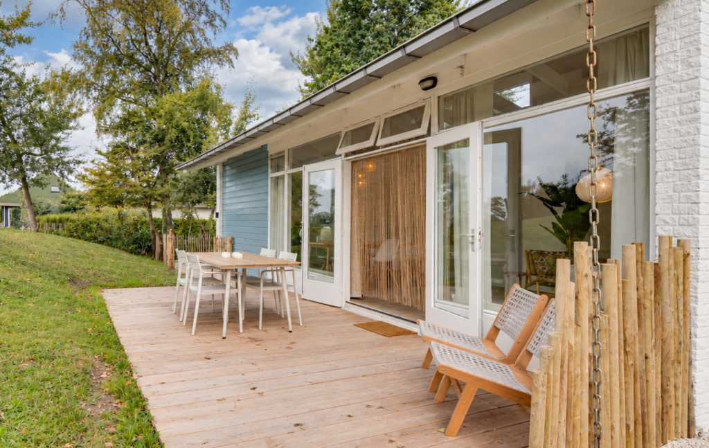 Openslaande deuren naar een ruim vlonderterras met eettafel en lounche-stoelen